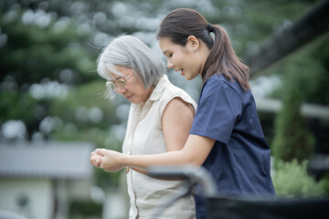Fototapeta premium Asian caregiver assisting elderly woman in wheelchair, providing compassionate rehabilitation, healthcare, trust, support, dignity, comfort, and happy family connection.