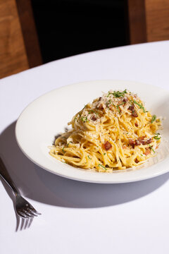 Creamy spaghetti carbonara with pancetta, parmesan cheese, and black pepper, Italian pasta dish three quarter angle on white tablecloth