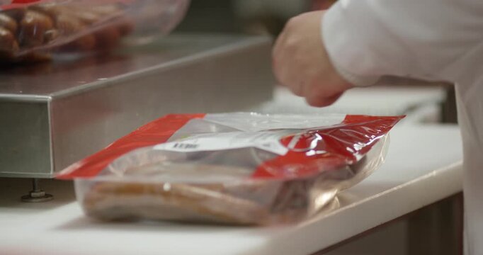 Sausages sealed in transparent plastic bags being weighed on a stainless steel scale at a food packaging station