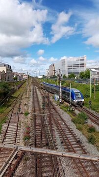 A blue TER passenger train travelling on railway tracks and approaching the station under cloudy sky in France. Great for public transport and travel concepts.