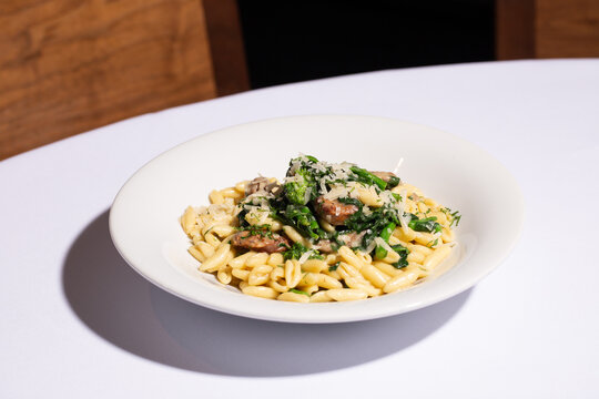 Angled close up shot of cavatelli pasta with sausage and broccoli rabe on a white tablecloth, restaurant table setting