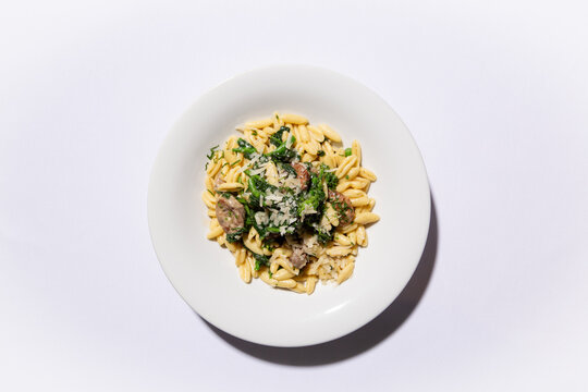 Overhead flat lay of cavatelli pasta with Italian sausage, broccoli rabe, and shaved parmesan on white plate, centered