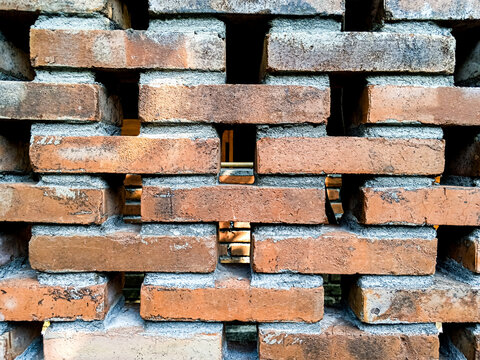 Openwork red brick wall forms a geometric ventilation pattern, photographed close up to show rustic masonry, gaps, mortar, and texture.
