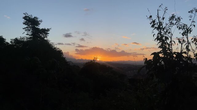Golden sunset over hills with silhouetted trees and city view