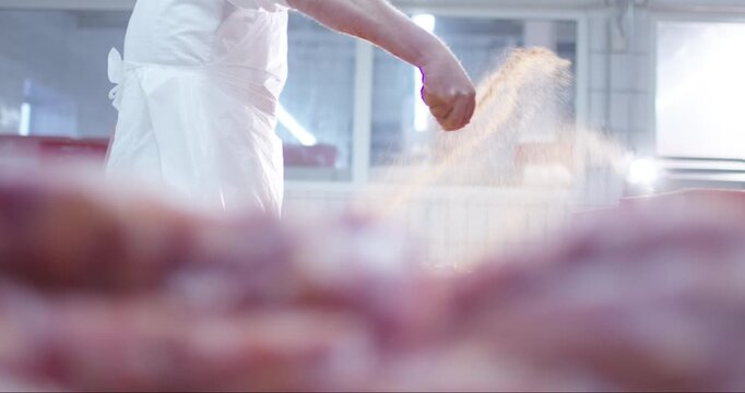 Butcher in white work clothes handles fresh meat in a bright processing plant with blurred foreground