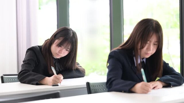 綺麗な新緑背景の教室で真剣にテストに取り組む日本人女子高校生複数　受験、定期テスト、模試の学生の動画