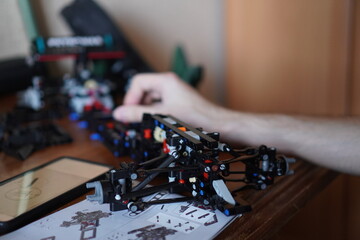 person assembling lego model on desk with instructions and parts close-up focused and creative hobby activity in crafting and diy setting with black and white plastic pieces. © Irina