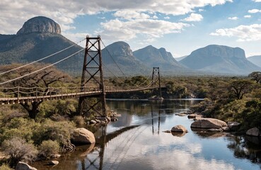 Fototapeta premium Steel suspension bridge over a calm river with mountain background