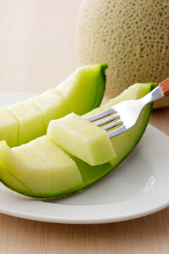 木目テーブルに置いた高品質な北海道産の青肉カットメロン　Slices of high-quality green flesh Japanese melon on a wooden table, premium Hokkaido muskmelon