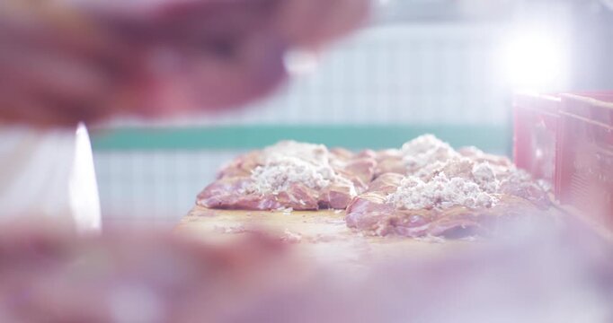 Hand reaching for seasoned meat pieces on a wooden work table in bright backlight at a meat processing facility