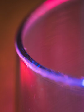 Macro abstract photography of a glass rim illuminated by vibrant blue and red neon light, creating a moody gradient effect