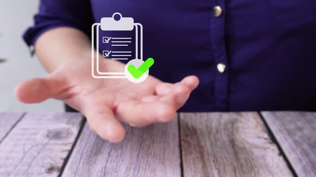 Close-up of a woman's hand at a table holding an animated clipboard icon and a checkmark