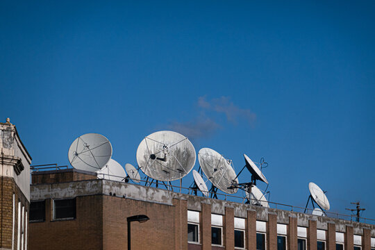 Parabolic antennas designed to receive or transmit radio wave information. They are mounted on a brick building under a clear blue sky