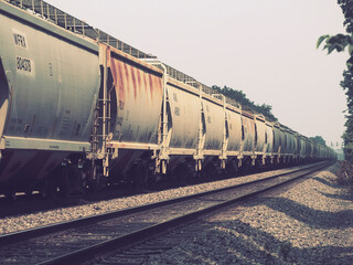 Long freight train with weathered hopper cars transporting bulk goods along railroad tracks on a hazy summer day © Donald