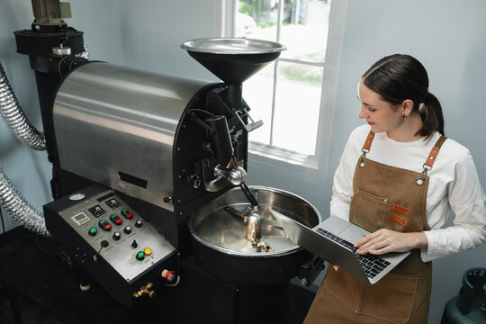 Female Coffee Roaster Managing Specialty Coffee Production on a Laptop Beside a Commercial Roasting Machine and Control Panel