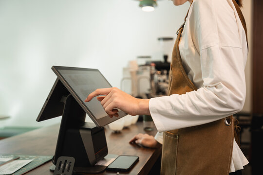Coffee Shop Barista Using a Touchscreen Point of Sale System at the Counter of a Modern Cafe and Independent Small Business