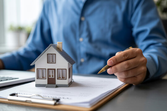 Professional realtor signing residential property agreement with small house model on desk at office.