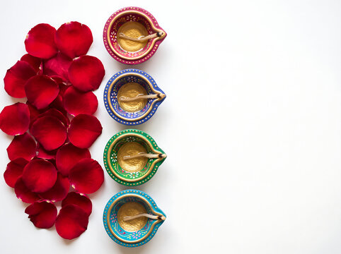  Top-down flat-lay of a minimalist Diwali still life with rose petals and colorful ceramic diyas with hand-painted designs on pure white background