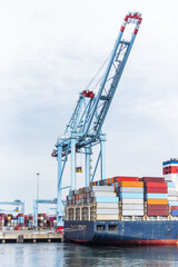 Obraz premium Modern container vessel docked at a commercial port while cranes load and unload shipping containers during routine terminal operations.