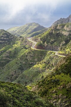 Landscape in the south-east of La Gomera near Vegaipala. Mountain slopes with palm trees and agaves, a road, sea, sun and clouds. La Gomera, Canary Islands, Spain