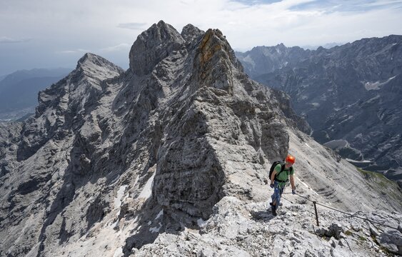 Mountaineer with helmet climbing in a secured climb on the rock, on a narrow rocky ridge, crossing the Jubil&auml;umsgrat, view of Rheintal and Alpspitze, Wetterstein range, Bavaria, Germany