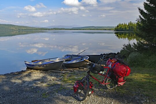 A lake with docked boats, a bicycle standing on the shore, surrounded by trees and under a cloudy sky, Viken, St&ouml;rlien, J&auml;mtland, Sweden