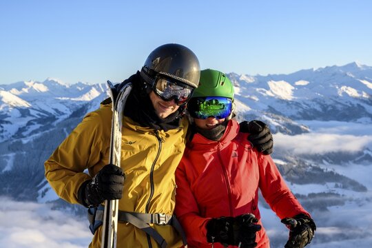 Two skiers with ski helmets and skis stand in front of a mountain panorama, couple, looking into the camera, SkiWelt Wilder Kaiser, Brixen im Thale, Tyrol, Austria