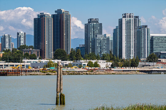 Construction and modern buildings rise over water of Frase River in South Vancouver under a clear blue sky