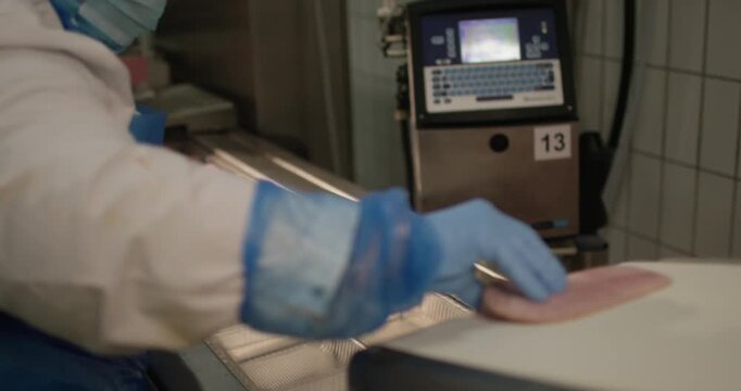 Gloved hand placing a slice of meat onto a conveyor line with an industrial labeling machine behind