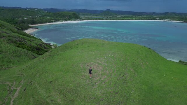 Woman Walking Ridge With Ocean View, Narrow Grassy Paths Snake Between Rolling Knolls Toward Distant Cove, Cinematic Composition With Moody Sea Horizon, Solitary Hike,Bukit Merese, Lombok, Tanjung Ann