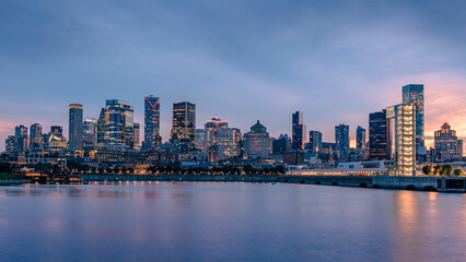 Fototapeta premium Montreal skyline at sunset seen from the Old Port, with downtown skyscrapers and the Port of Montreal Tower reflected in the Saint Lawrence River, Quebec, Canada