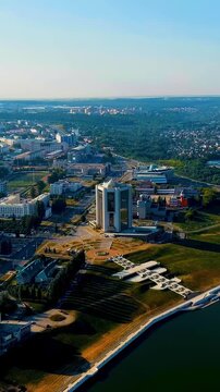Vertical video. Cheboksary, Russia. The Administration of the Head of the Chuvash Republic, a tall modern tower with reflective glass facade and a glass pyramid roof, aerial pull-back revealing Chebo