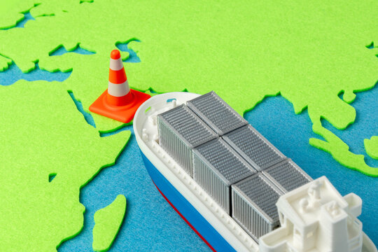 Miniature cargo ship facing a traffic cone on a green world map. Geopolitical trade conflicts, protectionist trade policies, embargoes concept.