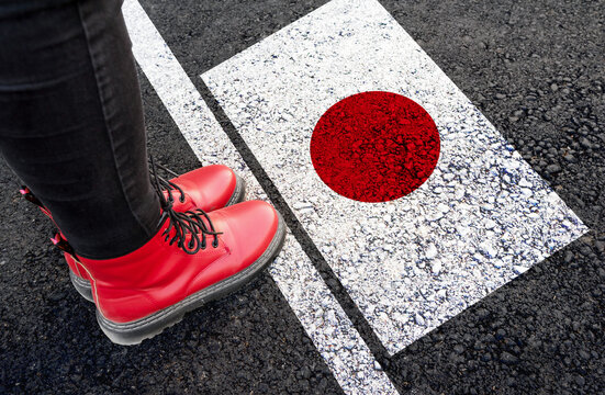 a woman with a boots standing on asphalt next to flag of Japan and border

