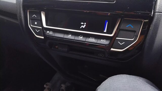 Asian man hand turns car AC off to on, increases fan speed, decreases temperature, then increases temperature for driving comfort in tropical weather