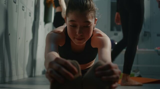 Dedicated Teenage Gymnast in Black Sports Top Bending Forward to Stretch Spine and Hamstrings. Concept of High Flexibility, Stamina, and Self Discipline Typical of Elite Youth Sports Training.