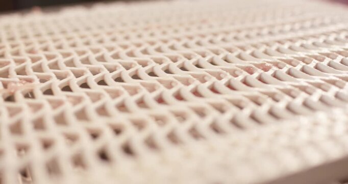 Thin slice of raw meat lying on a white plastic grid conveyor belt in a meat processing facility