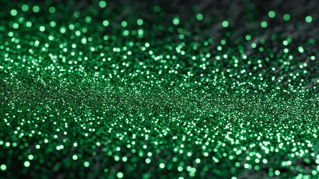 Shimmering green emerald glitter sparkles moving across a dark textured surface for festive celebratory backdrop