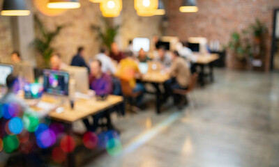 Fototapeta premium A blurred image of a modern office space with people working at wooden desks. Creative professionals collaborate around computers in a bright, industrial setting.
