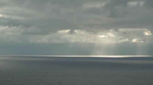 Crepuscular rays, ocean, clouds slowly moving across the horizon, casting dramatic sunbeams and bright light path onto the dark water.