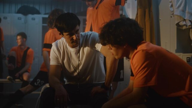 Football Coach Takes Moment to Motivate One of Teenage Players in Locker Room While Teammates Change Clothes Recover Nearby. Mentorship, Leadership, Strong Relationships that Shape Successful Teams.