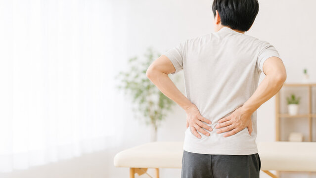 室内で腰を押さえる腰痛に悩む男性の後ろ姿