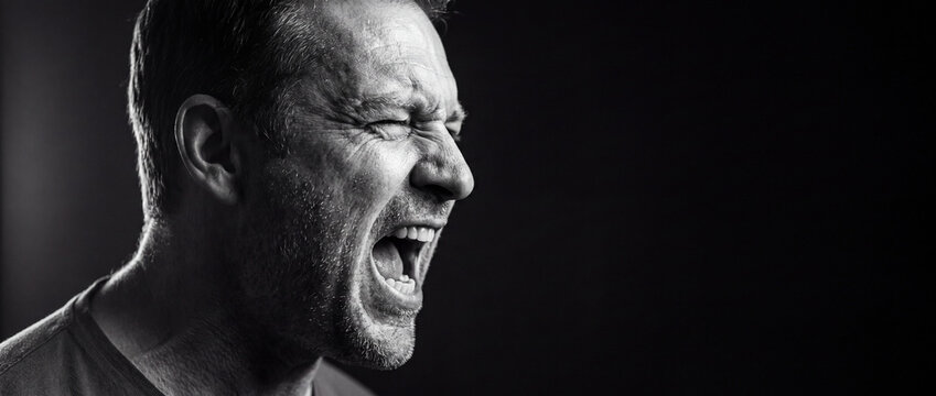 Angry man screaming in profile view, captured in a dramatic black and white portrait with intense facial expression and dark background, ideal for mental health and stress concepts