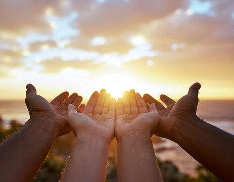 Close up of human hands opened up towards a beautiful bright golden sunset over the ocean, concept of hope, spirituality, faith, prayer, worship, and peace