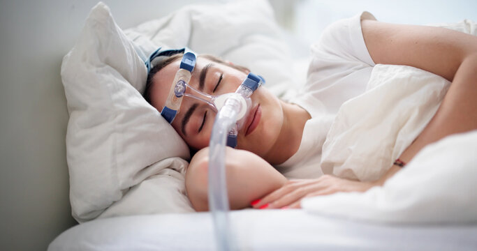 Young Woman Lying In Bed Wearing CPAP Mask