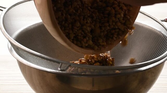 Close-up of a hand washing raw lentils and draining them in a strainer