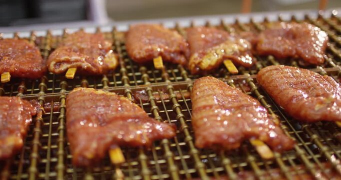 Rows of marinated meat pieces on wooden sticks lying on a wire rack with glossy glaze