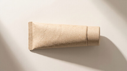 Obraz premium Blank eco-friendly cosmetic squeeze tube mockup made of recycled cardboard paper on beige background with soft natural shadows