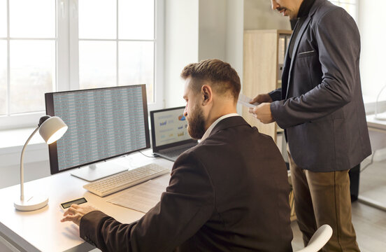 Accountants analysts conduct finance analysis in office. Two colleagues review data on a computer and prepare reporting documents to support budgets. Collaborative finance analysis in office.