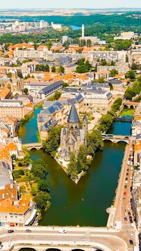 Vertical video. Metz, France. Temple Neuf, a Neo-Romanesque Protestant church with a dark stone spire, Drone footage over the Moselle River on a bright summer day. Drone footage, Point of interest. R